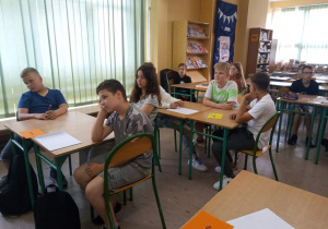 Uczestnicy konkursu siedzą przy stolikach w czytelni szkolnej.